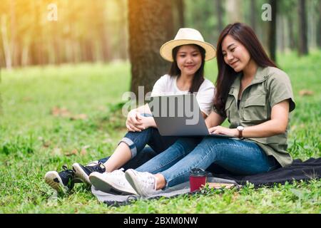 Due donne asiatiche che lavorano e utilizzano un computer portatile mentre si siedono nel parco Foto Stock