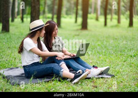 Due donne asiatiche che lavorano e utilizzano un computer portatile mentre si siedono nel parco Foto Stock