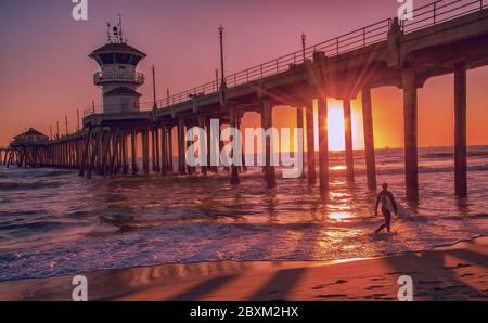 Silhouette di un surfer al tramonto di fronte al Huntington Beach Pier in California Foto Stock