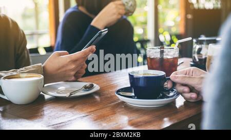 Immagine di primo piano di persone che usano il telefono cellulare e bevono caffè insieme in un caffè Foto Stock