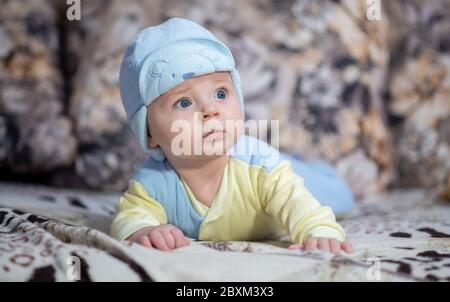 Bambino piccolo in pigiama e un cappello. Un bambino piccolo, un bambino, impara il mondo, si trova sul pancia, guarda via. Foto Stock