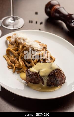 filetto di manzo con salsa e tagliatelle su tavola di legno con pepai e bicchiere di vino Foto Stock