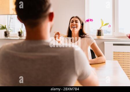 Bella giovane coppia ha un buon tempo insieme a casa mentre si mangia al tavolo che tiene i bastoni Foto Stock