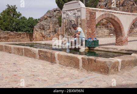 Uomo residente imbottigliare le bottiglie alla fontana Palomas Pillar costruita nel 16 ° secolo, Hornachos, Spagna. Stemma imperiale di a. Foto Stock