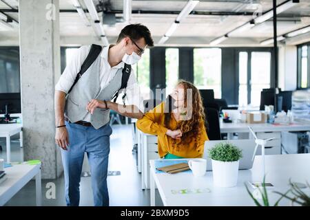 Giovani con maschere di fronte al lavoro in ufficio dopo blocco, saluto. Foto Stock