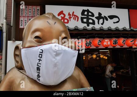 La statua di Billiken che indossa maschere facciali è vista al quartiere dello shopping e del divertimento di Shinsekai a Osaka, Japn il 6 giugno 2020. Foto Stock