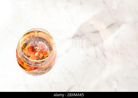 Il tè floreale in fiore viene servito in un bicchiere di vino, tavolo in marmo bianco presso il cafe' alla moda. Festa del tè di lusso, tè creativo che serve concetto. Posiziona per il testo Foto Stock