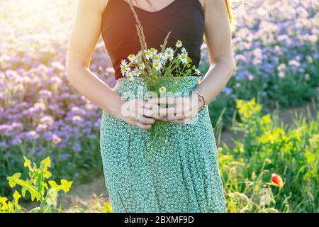 Donna che ama la natura mentre cammina sui campi selvaggi con un bouquet di fiori selvatici Foto Stock