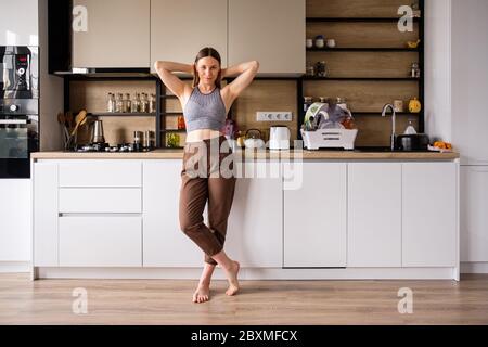 Atmosfera mattutina in una cucina moderna. Bella donna si alza in posa e rilassante. Cucina moderna donna Foto Stock