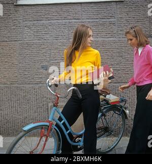 Negli anni '70. Due giovani donne vestite in stile e colori tipici degli anni '70. La ragazza nel ponticello giallo ha una vecchia bicicletta e i suoi libri di studio con lei. Svezia giugno 19 1972. Foto Stock