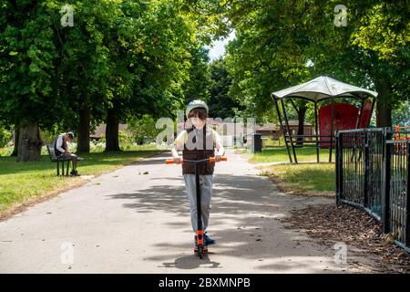 Un ragazzo cavalcava il suo scooter attraverso il parco locale lungo un tranquillo sentiero. Foto Stock