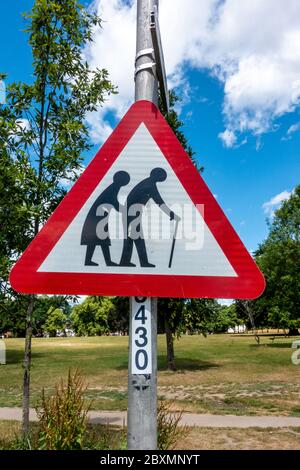 Un cartello rosso triangolare in un parco avverte le persone di pedoni che potrebbero essere lenti o instabili a causa della vecchiaia o di essere inabili. Foto Stock