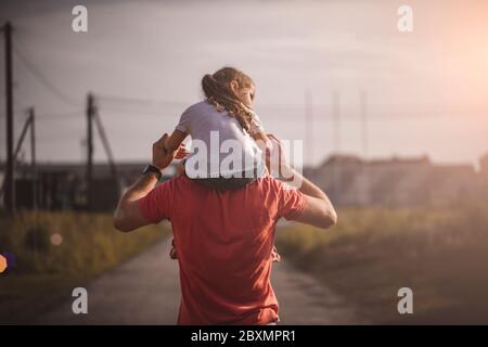 Papà danzando sulle spalle con sua figlia al sole. Padre viaggia con il bambino sulle spalle ai raggi del tramonto. Bambini con i genitori camminano al tramonto Foto Stock