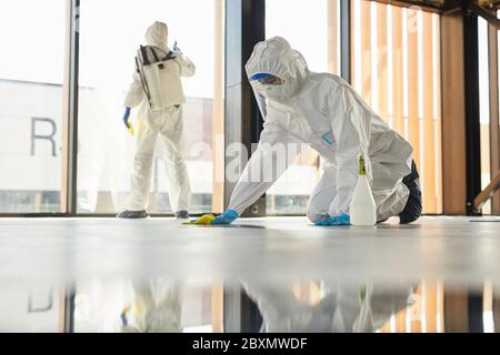 Ritratto a lunghezza intera di due operatori che indossano tute di protezione per la pulizia delle superfici in interni durante la disinfezione, spazio di copia Foto Stock