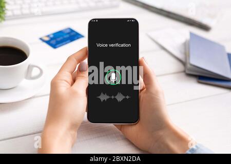 Mani femminili che tiene lo smartphone utilizzando l'applicazione di riconoscimento vocale seduto in interni Foto Stock
