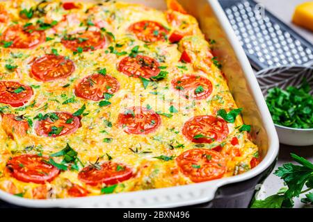 Frittata tradizionale all'uovo con pomodori e formaggio nel piatto del forno, vista dall'alto. Frittata al forno con verdure e formaggio. Foto Stock