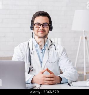 Lavorare a casa online. Il medico si siede al tavolo con il computer portatile all'interno Foto Stock