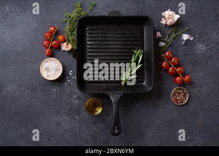 Padella piatta vista dall'alto in ghisa nera per barbecue. Padella con ingredienti da cucina e spezie su fondo di cemento con spazio per la copia Foto Stock