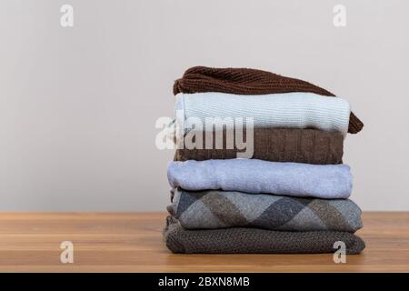 Un mucchio di maglioni caldi su un tavolo di legno su uno sfondo chiaro. Abiti autunnali e invernali Foto Stock