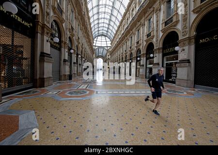 Un uomo che fa jogging nel vuoto della Galleria Vittorio Emanuele con negozi chiusi durante la chiusura del Covid-19 a Milano. Foto Stock