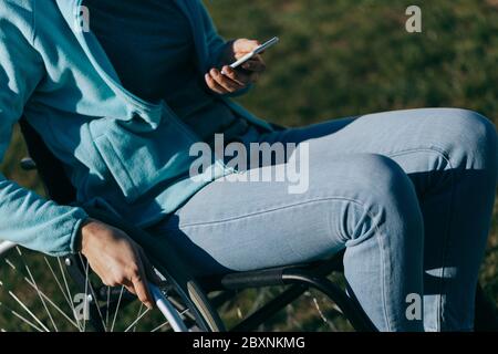 Una donna in sedia a rotelle con un telefono in mano cammina per strada, la sua mano è vicina, un irriconoscibile Foto Stock