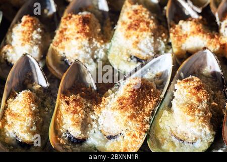 Cozze cotte con parmigiano, pangrattato e burro di erbe. Cibo di fondo. Cucina mediterranea. Concetto per un pasto gustoso e sano. Primo piano. Foto Stock