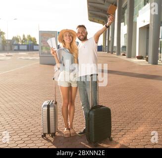 Coppia entusiasta che mostra i biglietti vicino all'aeroporto moderno Foto Stock