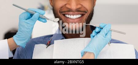 Un dentista con le mani tagliate e gli attrezzi e un paziente sorridente Foto Stock