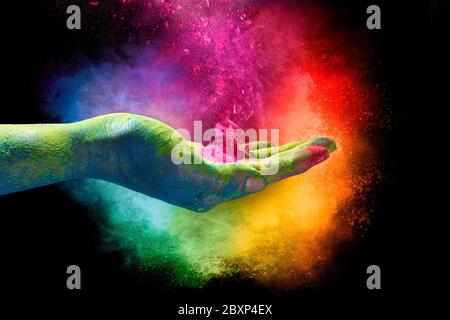 Polvere magica di colore arcobaleno che esplode dal palmo di una mano a cupola creando una nuvola vibrante di polvere nei colori dello spettro su una ba nera Foto Stock