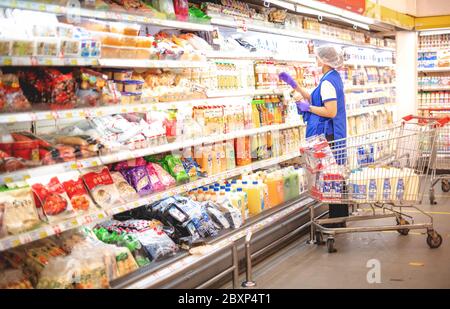 BANGKOK / THAILANDIA - MAGGIO 31 2020: Il supermarket operaio indossare uniforme e guanto chirurgico disporre cibo congelato in frigorifero, la preparazione di alimenti Foto Stock