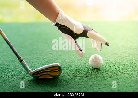 Mano femminile indossando guanti professionali bianchi con la mano sinistra che mette il golfball e il golf putter sul campo di erba che si prepara a colpire il ba di golf Foto Stock