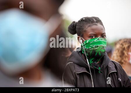 Giovane donna, con grappoli di capelli, indossa una maschera a fantasia e auricolari bianchi alla protesta Black Lives Matter UK. Hyde Park, Londra, Inghilterra, Regno Unito Foto Stock