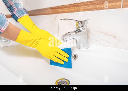 Pulizia in bagno. Una donna pulisce il lavello e il rubinetto del lavabo. Foto Stock
