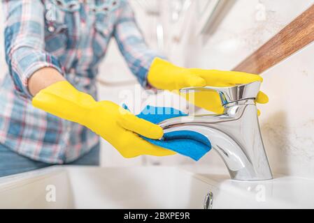 Pulizia in bagno. Una donna pulisce il lavello e il rubinetto del lavabo. Foto Stock