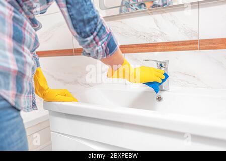 Pulizia in bagno. Una donna pulisce il lavello e il rubinetto del lavabo. Foto Stock