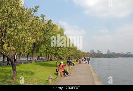 Lago occidentale di Hangzhou, provincia di Zhejiang, Cina. Persone sedute sul lago sulla strada rialzata di Baidi. Foto Stock