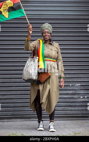 Ritratto di una donna di mezza età, si trovava di fronte a un otturatore di sicurezza in metallo, indossando abiti africani e con una bandiera. Londra UK Foto Stock
