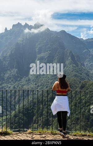 Giovane donna adulta che guarda le cime delle montagne dal balcone punto panoramico Balcoes levada. Isola di Madeira, Portogallo. Foto Stock