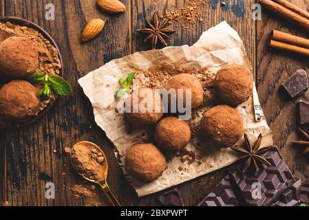 Tartufi al cioccolato con cacao in polvere, cannella, mandorle su sfondo di tavola in legno. Tartufo caramella al cioccolato fatto in casa Foto Stock