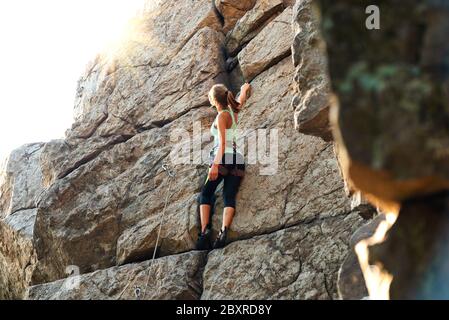 Bella donna arrampicata sulla High Rock al tramonto Foggy nelle montagne. Concetto di avventura ed Extreme Sport Foto Stock