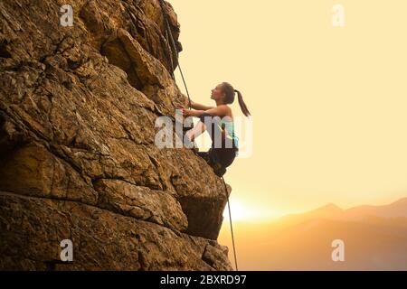 Bella donna arrampicata sulla High Rock al tramonto Foggy nelle montagne. Concetto di avventura ed Extreme Sport Foto Stock