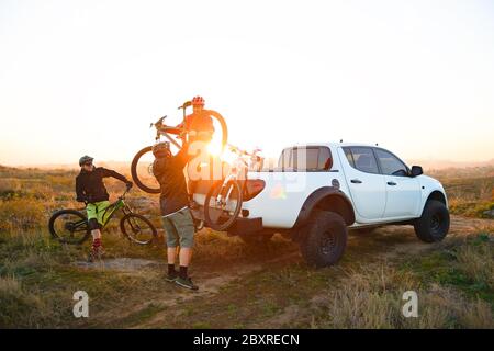 Amici ciclisti prepararsi per l'equitazione in bicicletta e prendere le biciclette dal pick-up Offroad camion in montagna al caldo tramonto d'autunno. Avvento MTB Foto Stock