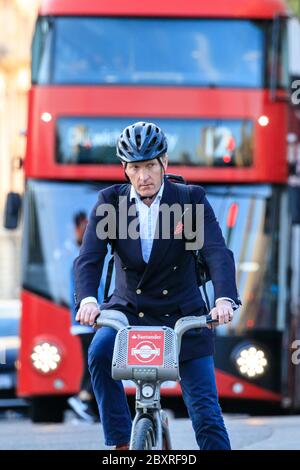Adatto ciclista maschile della città sul noleggio bici davanti al bus rosso a Westminster, Loondon, Regno Unito Foto Stock
