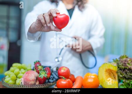 Medico nutrizionista che tiene il cuore rosso con frutta e verdura varie. Foto Stock