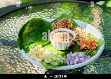 Miang kham, un antipasto reale a foglia, è un tradizionale spuntino del Sud-est asiatico dalla Thailandia e dal Laos. È sul piatto bianco in tavolo esterno con Foto Stock