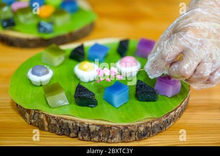 La mano dello chef tailandese sta decorando le varietà tradizionali e colorati dessert thailandesi, farina fumante, crema di crema nera, crema di cocco e fagioli fumanti, strato Foto Stock