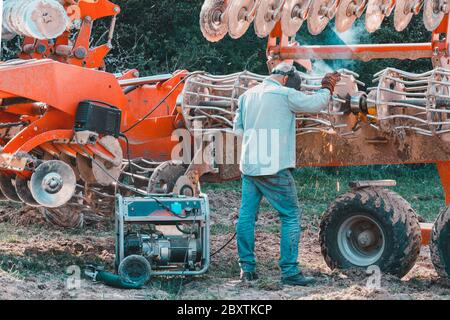 L'agricoltore ripara i erpici se sono danneggiati colpendo pietre. Una saldatrice principale salda parti metalliche di attrezzature agricole. Foto Stock