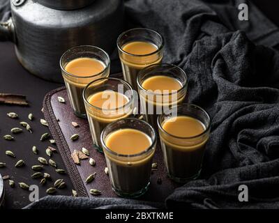 Chai indiano in tazze di vetro con bollitore di metallo e altre masala per preparare il tè. Foto Stock