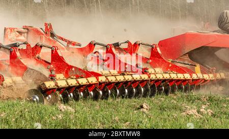 L'attrezzatura agricola riduce la terra arata. Un trattore cingolato tira un erpice per allentare il terreno da vicino. Foto Stock