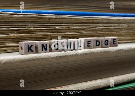 Primo piano di conoscenza di parola isolata scritto da piastrelle di legno di lettera su palo con vecchi libri gialliti Foto Stock
